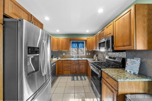 kitchen with light stone countertops, light tile patterned floors, appliances with stainless steel finishes, brown cabinetry, and a sink