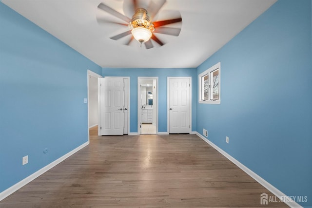 unfurnished bedroom featuring a ceiling fan, ensuite bath, wood finished floors, and baseboards