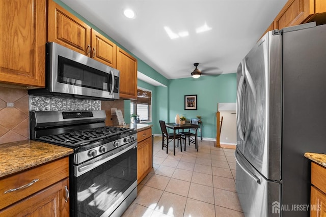 kitchen featuring a ceiling fan, backsplash, stainless steel appliances, brown cabinetry, and light tile patterned floors