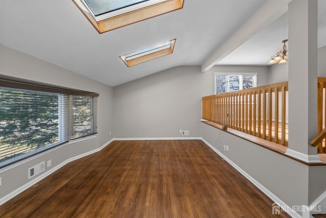 empty room with visible vents, lofted ceiling with skylight, wood finished floors, baseboards, and a chandelier