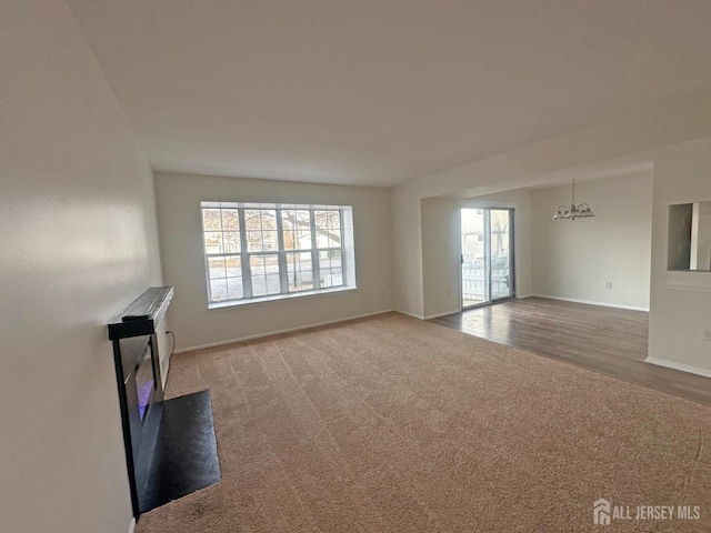 unfurnished living room with baseboards, carpet, wood finished floors, and a chandelier