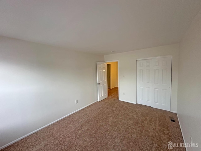 unfurnished bedroom featuring carpet floors, baseboards, a closet, and visible vents