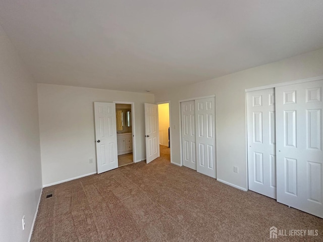 unfurnished bedroom featuring carpet flooring, multiple closets, baseboards, ensuite bathroom, and visible vents