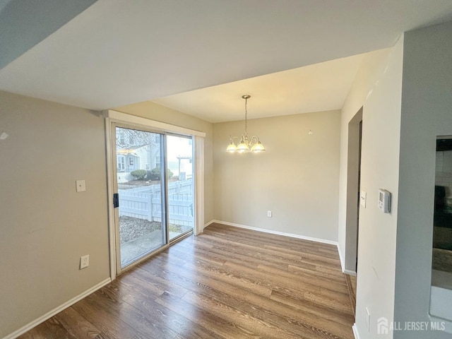 unfurnished dining area featuring an inviting chandelier, baseboards, and wood finished floors