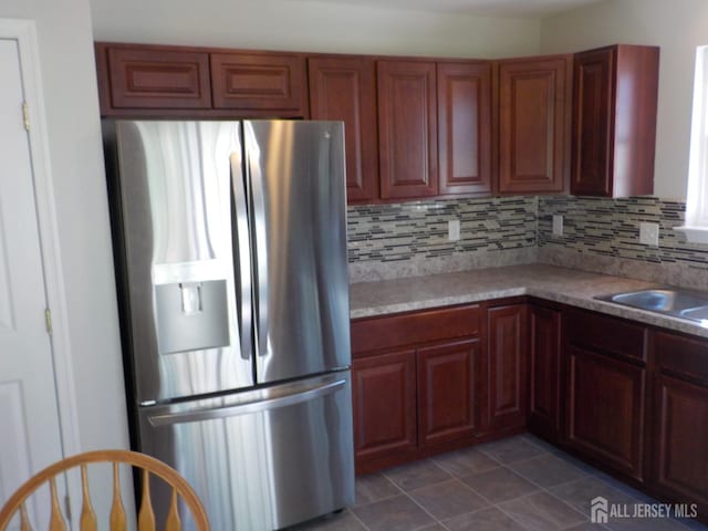 kitchen featuring stainless steel refrigerator with ice dispenser, tasteful backsplash, light countertops, and a sink