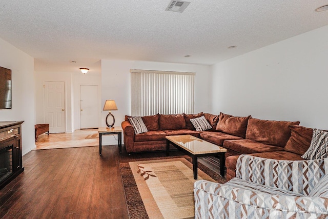 living area featuring a textured ceiling, hardwood / wood-style floors, a fireplace, and visible vents