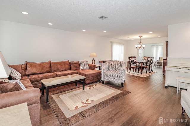 living area with a textured ceiling, a notable chandelier, recessed lighting, dark wood-type flooring, and visible vents