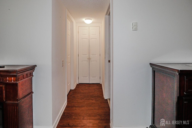 hall featuring a textured ceiling, baseboards, and wood finished floors