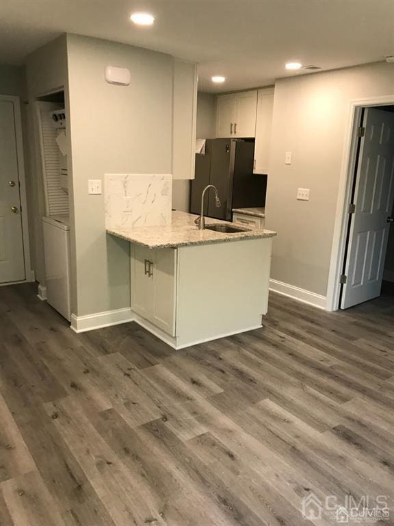 kitchen featuring a peninsula, a sink, white cabinetry, freestanding refrigerator, and dark wood-style floors