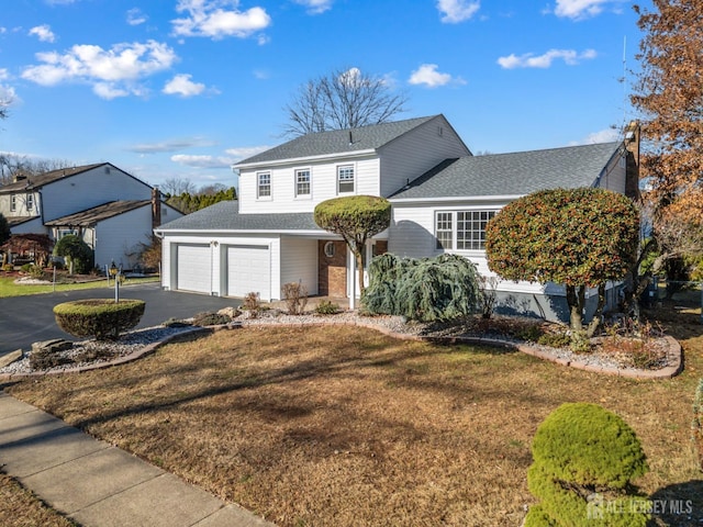 traditional-style house with a garage, aphalt driveway, a front lawn, and a shingled roof