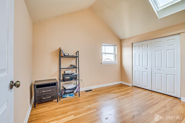 bedroom with wood finished floors, visible vents, baseboards, vaulted ceiling with skylight, and a closet