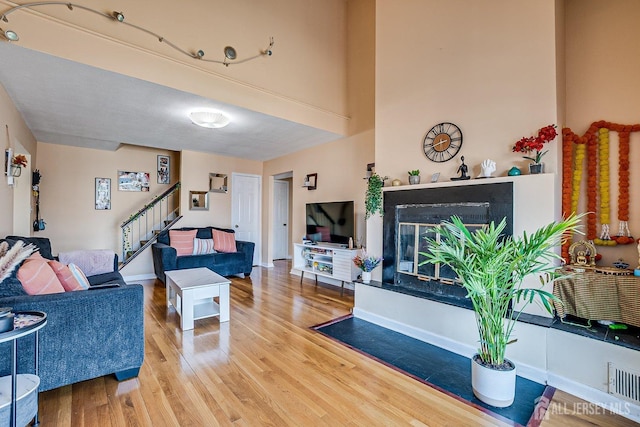 living room with visible vents, a glass covered fireplace, wood finished floors, stairway, and baseboards