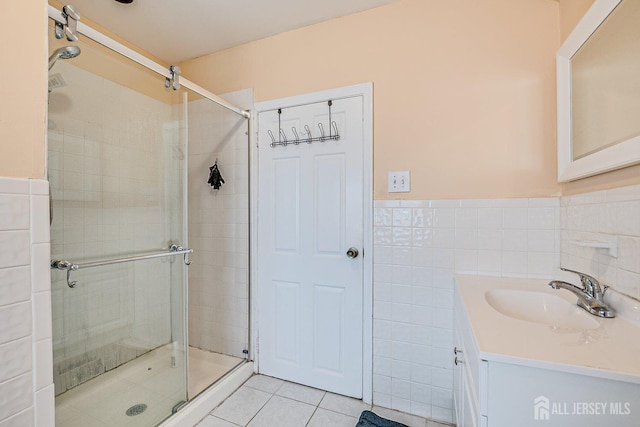 full bathroom with a wainscoted wall, tile walls, a shower stall, tile patterned flooring, and vanity