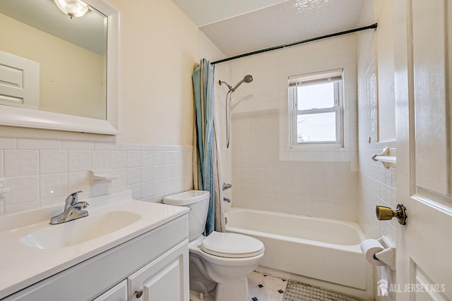 bathroom with a wainscoted wall, toilet, vanity, shower / tub combo, and tile walls