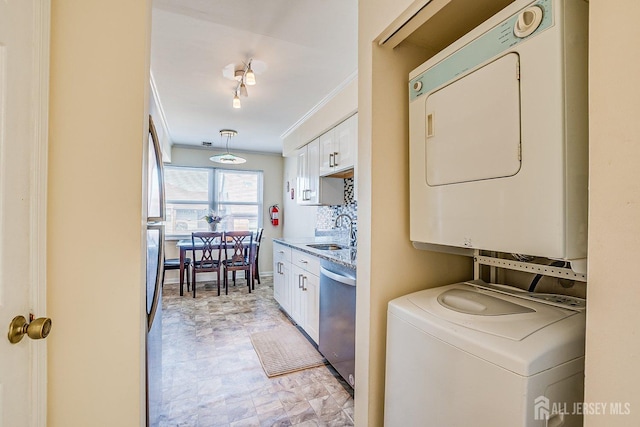 laundry room with stacked washer and dryer, a sink, rail lighting, crown molding, and baseboards