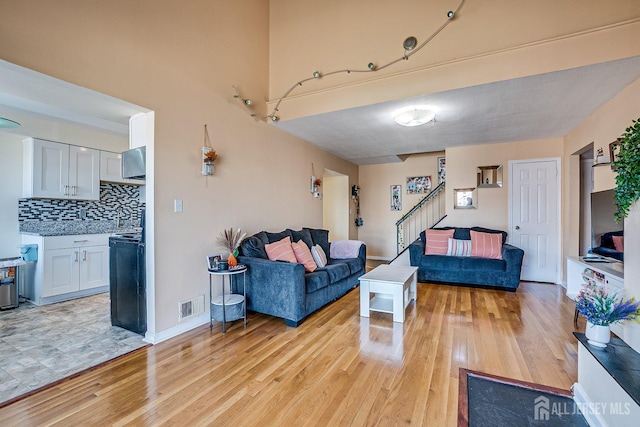 living area with visible vents, light wood-type flooring, stairs, and baseboards