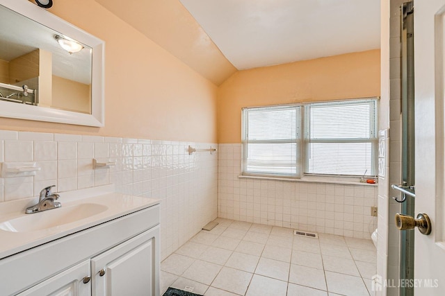 full bath with tile patterned floors, tile walls, vanity, and vaulted ceiling