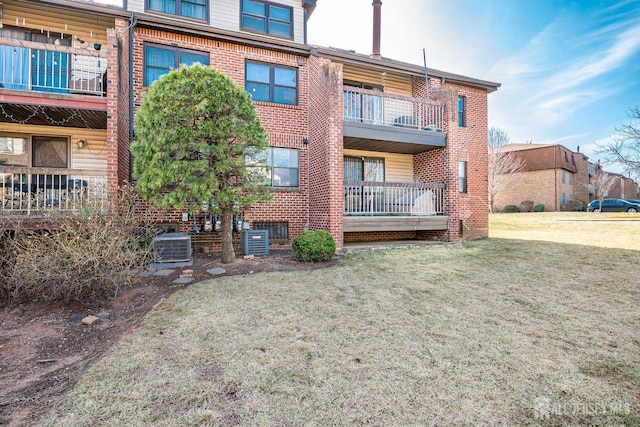 rear view of house featuring brick siding, central AC, and a yard