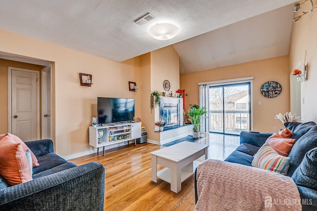 living area featuring visible vents, baseboards, lofted ceiling, light wood-style flooring, and a textured ceiling