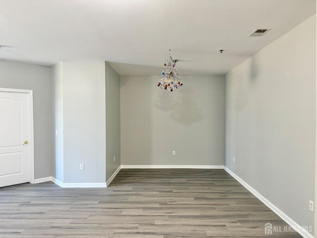 spare room with visible vents, baseboards, a notable chandelier, and wood finished floors