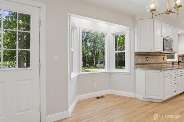 3 Cedar Ln, Milltown, NJ 08850 - kitchen featuring a chandelier, stainless steel microwave, white cabinets, light wood-style floors, and light stone countertops