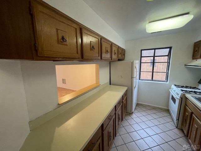 kitchen featuring white appliances, brown cabinets, range hood, light countertops, and light tile patterned flooring