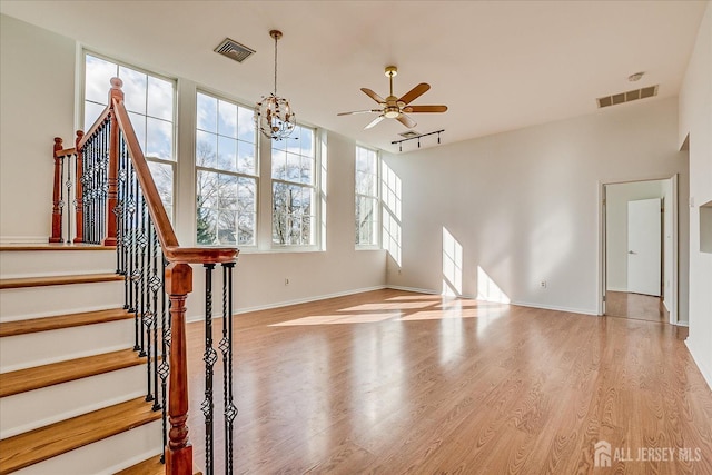 unfurnished living room with ceiling fan with notable chandelier, light hardwood / wood-style flooring, and track lighting