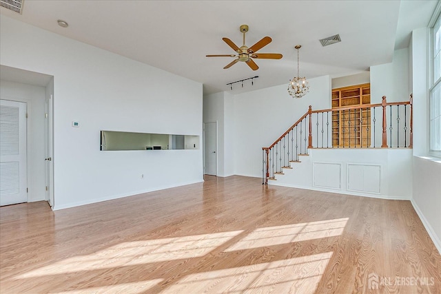 unfurnished living room with ceiling fan with notable chandelier, track lighting, and light hardwood / wood-style floors