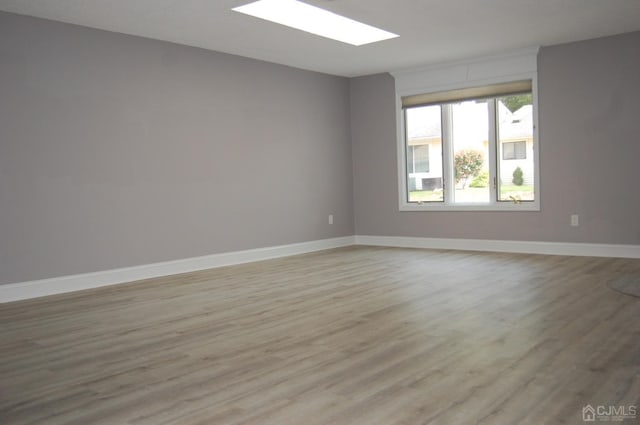 empty room featuring a skylight, baseboards, and light wood finished floors