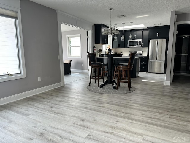 kitchen featuring a breakfast bar, stainless steel appliances, visible vents, light wood-style flooring, and dark cabinets