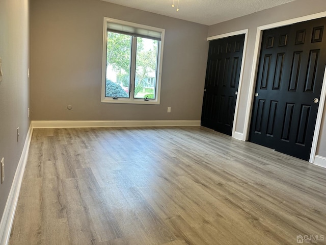 unfurnished bedroom with baseboards, two closets, and wood finished floors