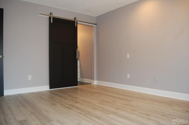 empty room with light wood finished floors, a barn door, and baseboards