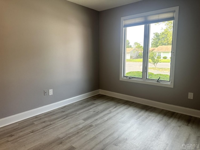 unfurnished room with plenty of natural light, wood finished floors, and baseboards