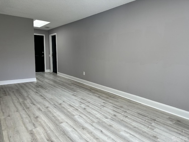 unfurnished room with a skylight, a textured ceiling, baseboards, and wood finished floors