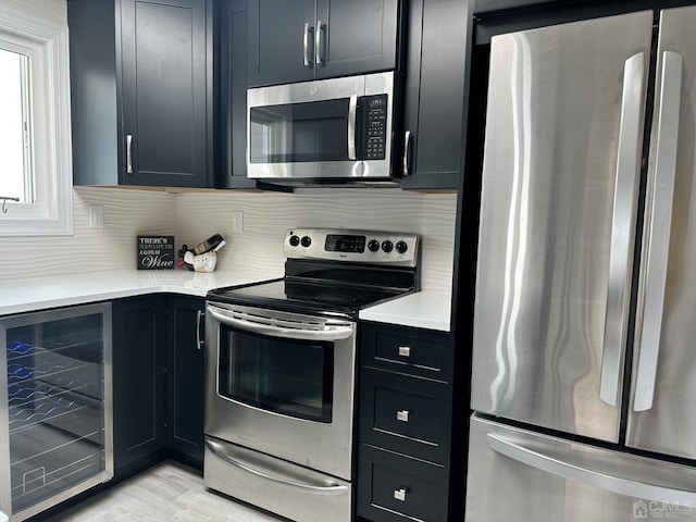 kitchen with beverage cooler, decorative backsplash, stainless steel appliances, light countertops, and light wood-type flooring