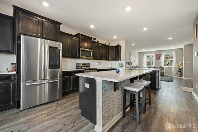 kitchen with hardwood / wood-style flooring, stainless steel appliances, a kitchen island, a kitchen breakfast bar, and dark brown cabinetry