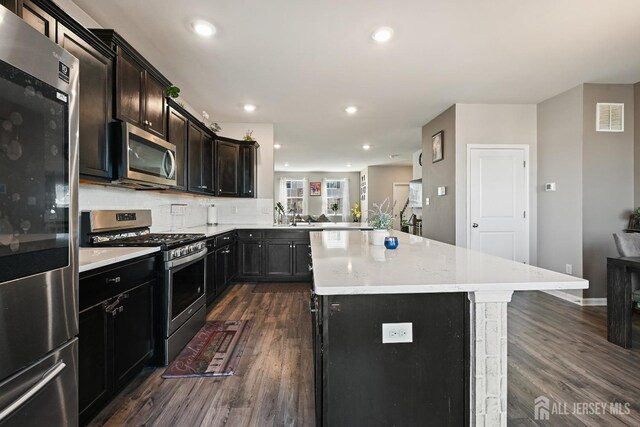 kitchen featuring kitchen peninsula, a center island, stainless steel appliances, backsplash, and dark hardwood / wood-style flooring