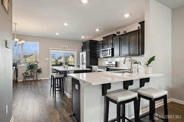 kitchen featuring a chandelier, stainless steel appliances, dark hardwood / wood-style flooring, a breakfast bar area, and sink