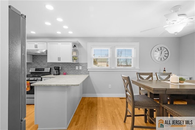 kitchen featuring tasteful backsplash, white cabinets, fridge, kitchen peninsula, and gas stove