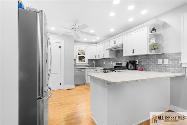 kitchen with light hardwood / wood-style flooring, appliances with stainless steel finishes, white cabinetry, light stone counters, and kitchen peninsula