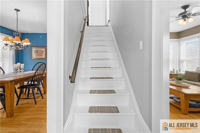 stairs with ceiling fan with notable chandelier and hardwood / wood-style floors