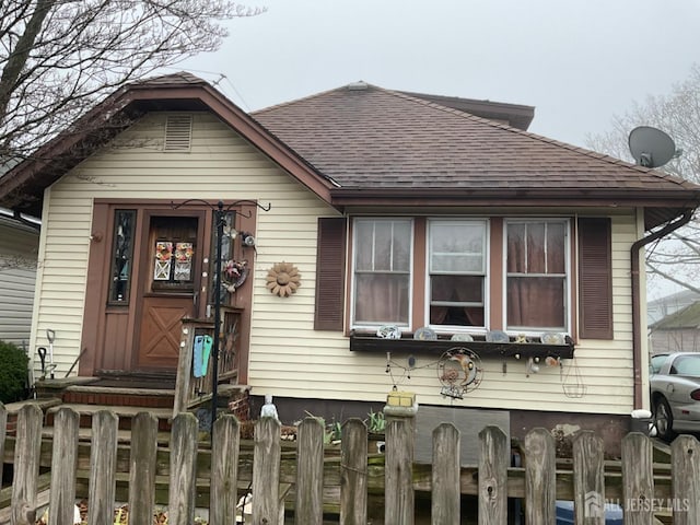 view of front facade with roof with shingles and fence