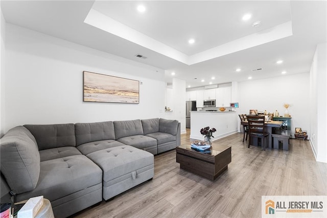 living area featuring recessed lighting, visible vents, baseboards, a tray ceiling, and light wood finished floors