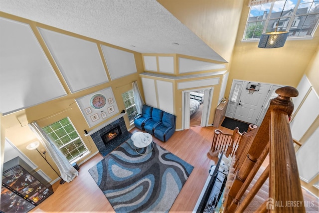 living room with a towering ceiling, wood finished floors, a warm lit fireplace, plenty of natural light, and a textured ceiling