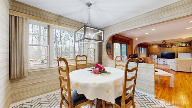 dining space with arched walkways, a wealth of natural light, a notable chandelier, and wallpapered walls