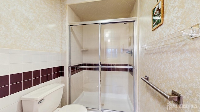 bathroom with a shower stall, toilet, and tile walls