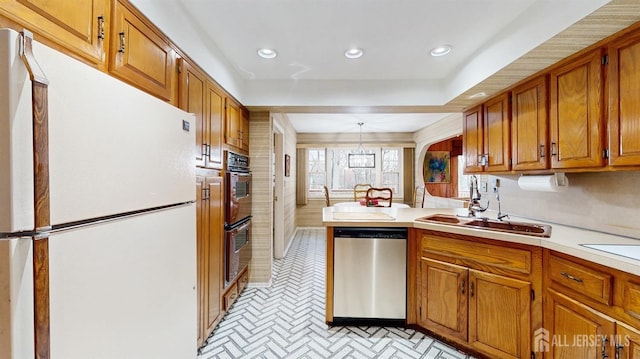 kitchen with brown cabinets, light countertops, stainless steel dishwasher, a sink, and freestanding refrigerator