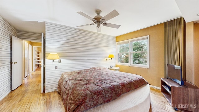 bedroom featuring wood-type flooring, wood walls, and a ceiling fan