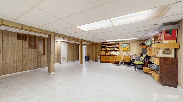 finished basement featuring a drop ceiling, baseboards, wood walls, and tile patterned floors