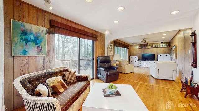 living area with arched walkways, wood finished floors, wood walls, and ceiling fan